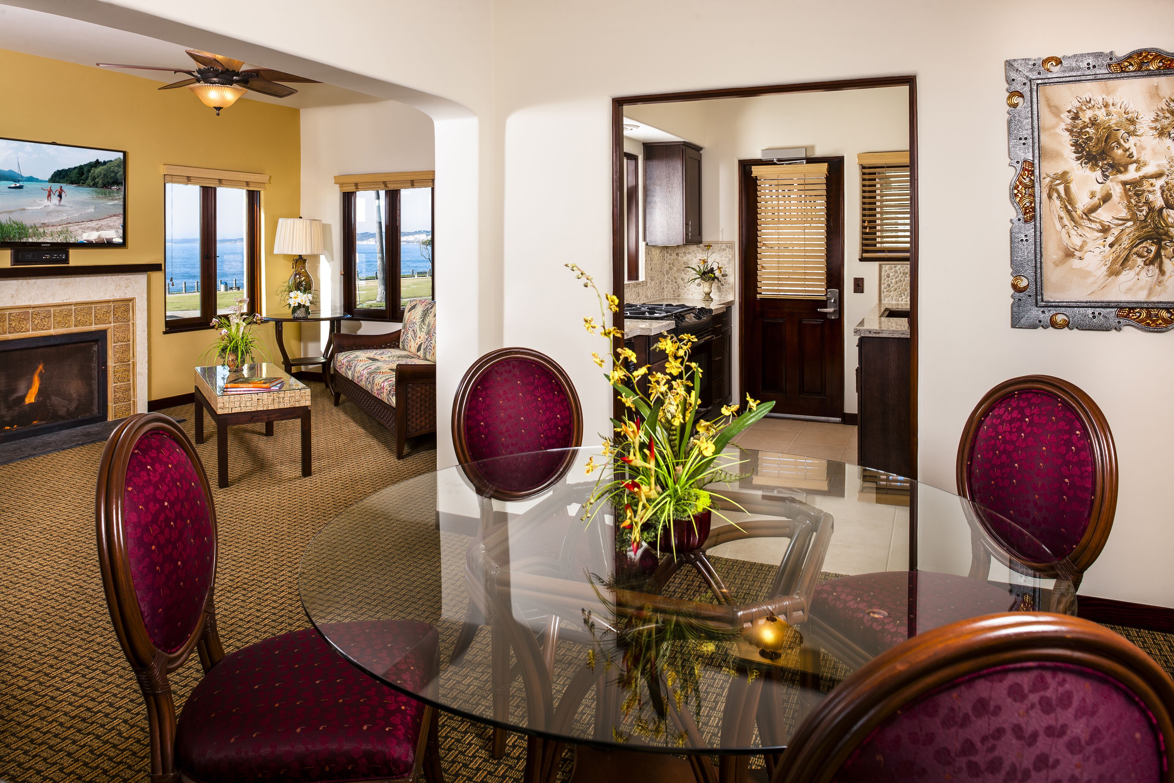 A dining area with a glass table, purple upholstered chairs, and a vase with flowers.