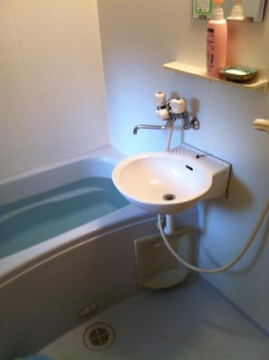 Et badeværelse med en hvid vask, badekar og en hylde med toiletartikler.