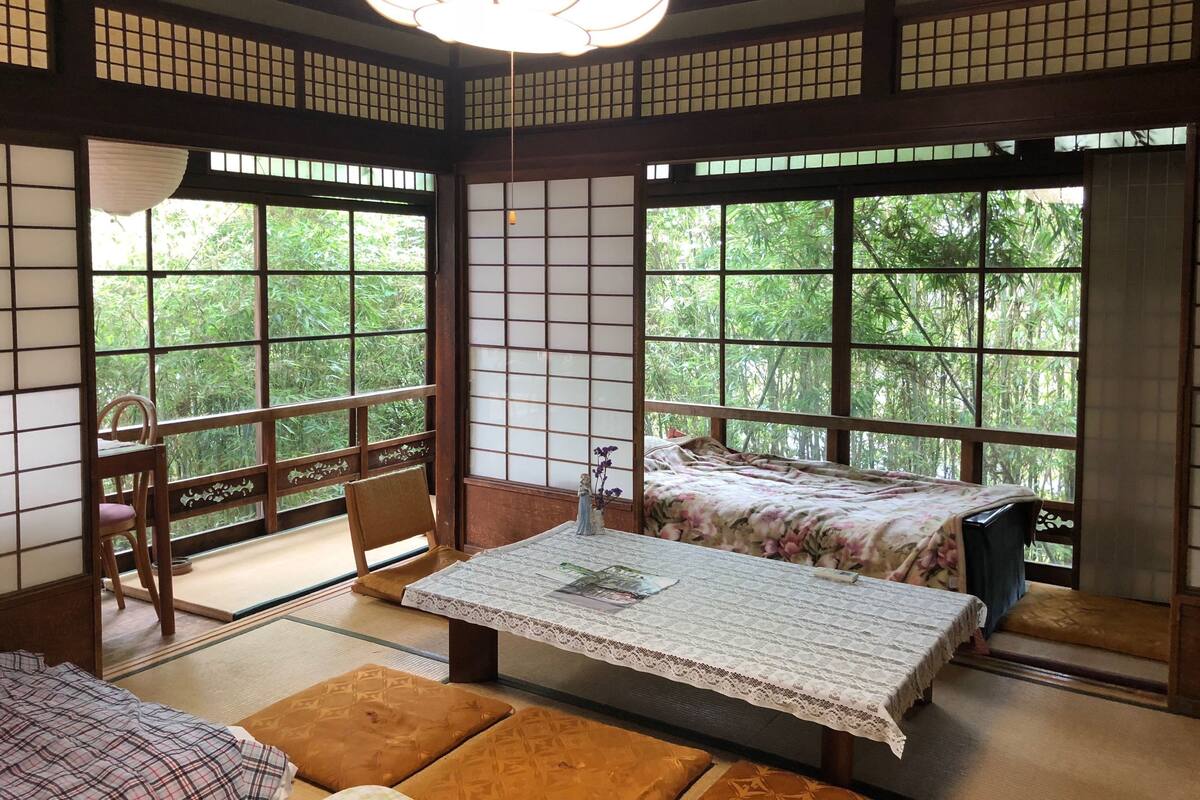 Una habitación tradicional japonesa con suelo de tatami, una mesa baja con mantel de encaje y una cama con colcha estampada con motivos florales.