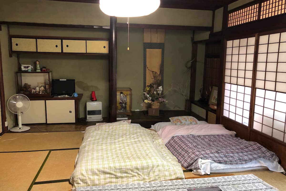 Una habitación tradicional japonesa con suelo de tatami, futón, escritorio con ordenador, ventilador y celosía shoji.