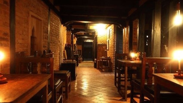 Un couloir étroit aux murs de briques, avec des tables et des chaises en bois.