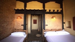 Une chambre avec deux lits simples, des poutres en bois, des murs en briques et deux lampes fixées au mur.