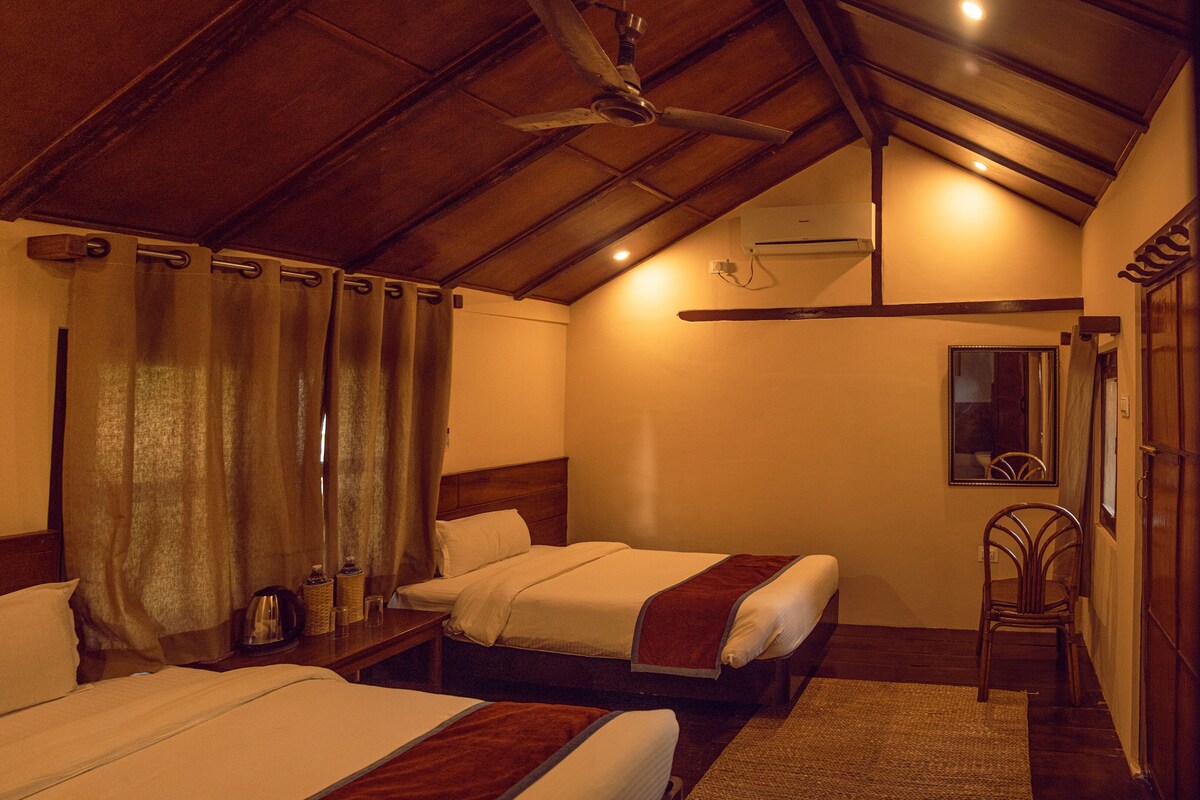 Habitación de hotel con dos camas, ventilador de techo, aire acondicionado, un espejo y una silla de madera.