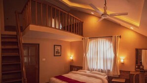 A bedroom with a large bed, a ceiling fan, a staircase, and a desk with a chair. - Safari Adventure Lodge (Sauraha)