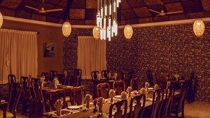 A dining area with wooden tables and chairs, a stone wall, and hanging wicker lamps. - Safari Adventure Lodge (Sauraha)