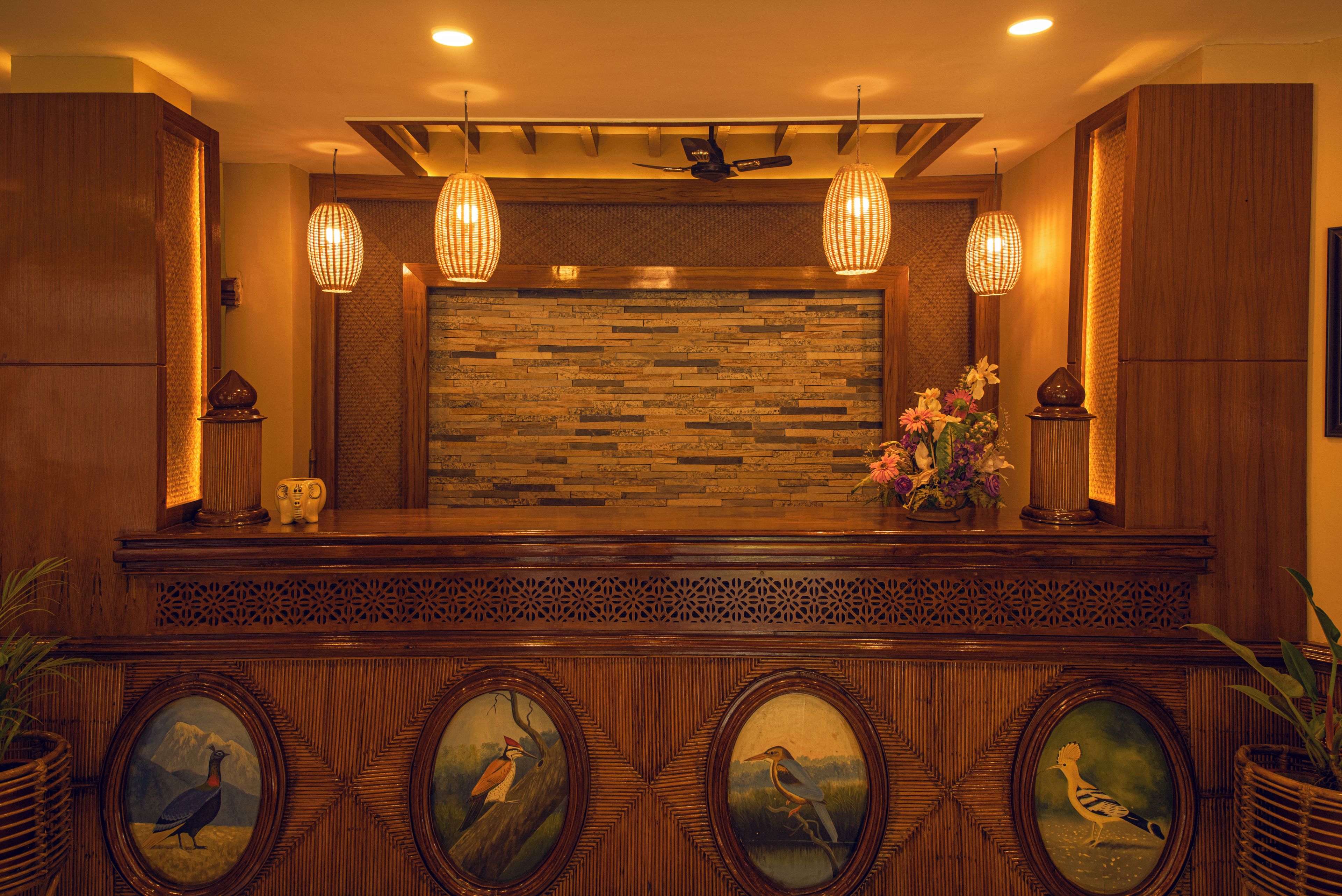 A reception desk with a wooden finish, a stone wall backdrop, and framed bird paintings.