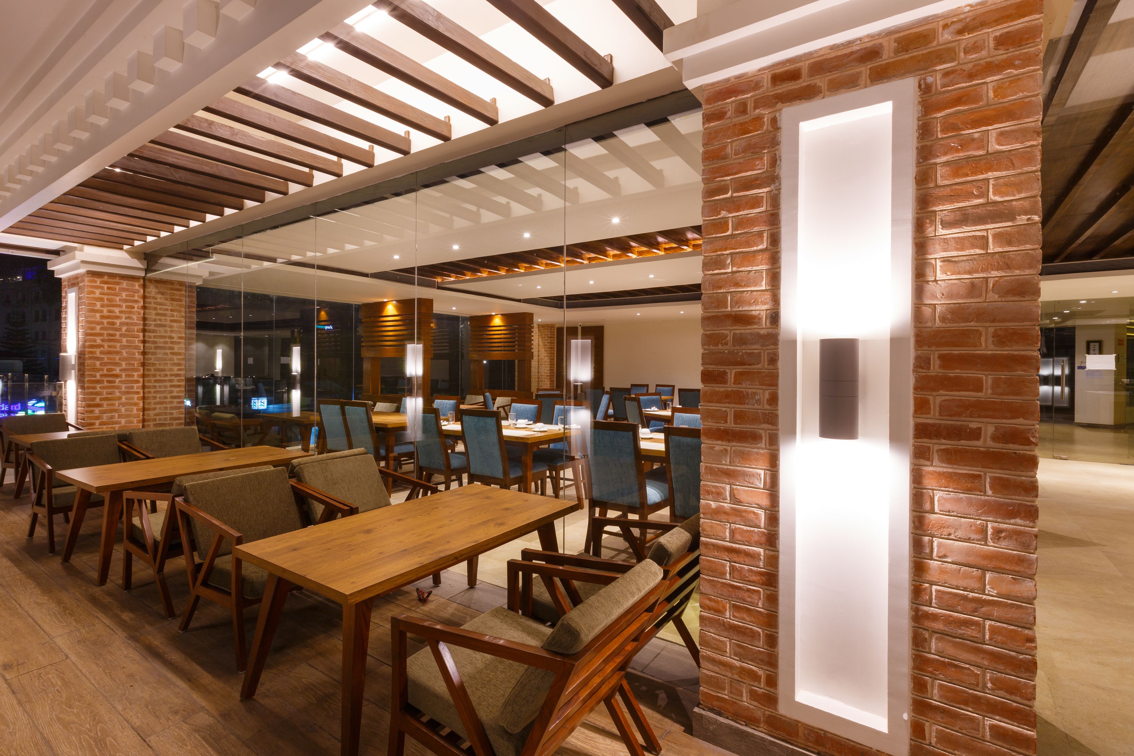A modern indoor dining area with brick walls, wooden tables, and blue chairs.