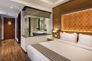 A hotel room with a large bed, a bathroom with a glass shower enclosure, and a wooden headboard with a floral pattern.