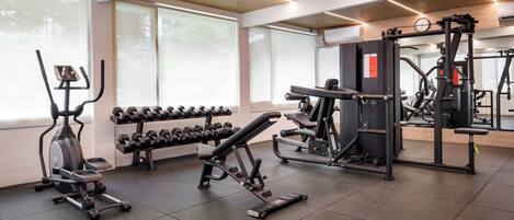 A gym with exercise equipment, dumbbells, and large windows.