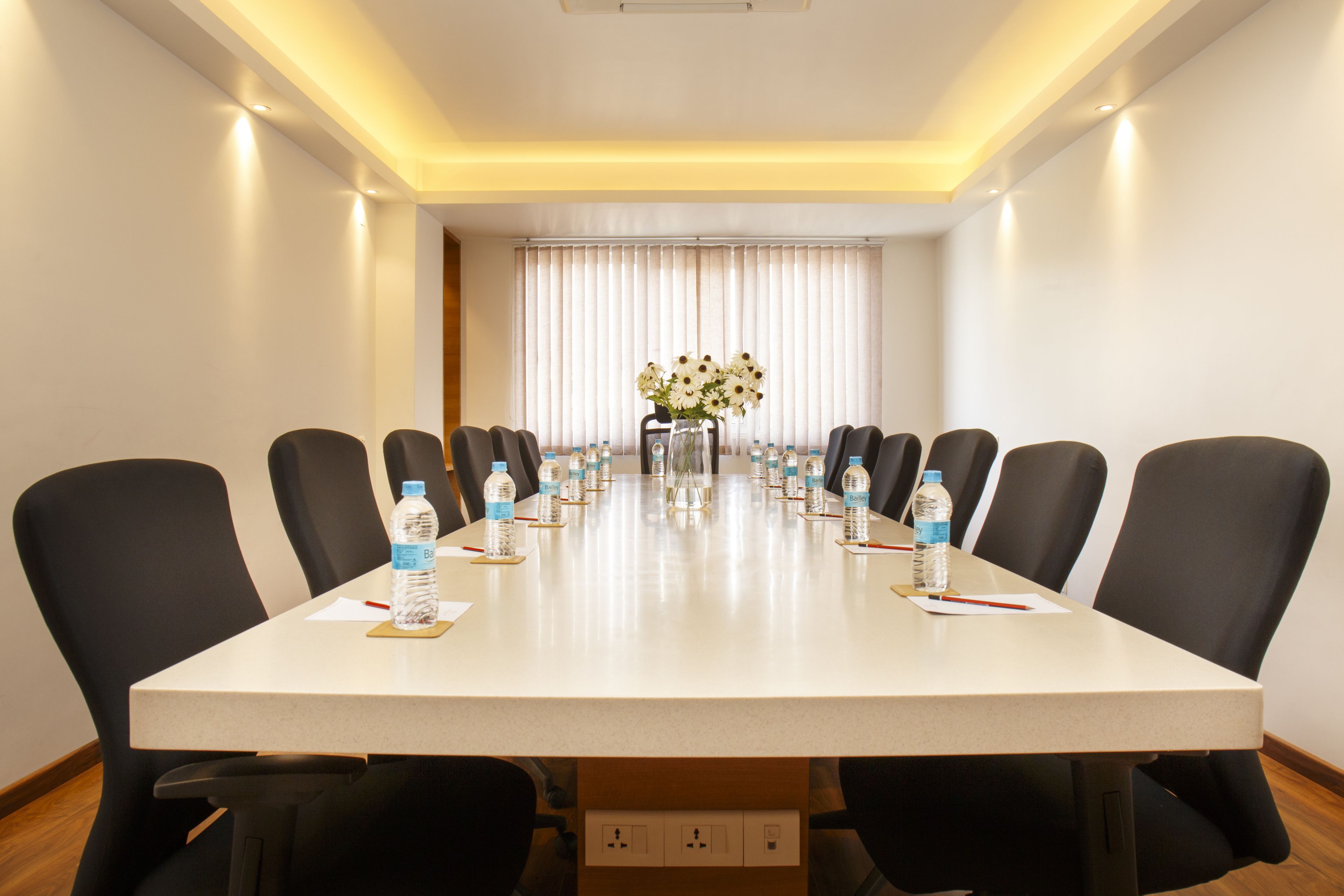 A conference room with a long table, black chairs, water bottles, and a vase of flowers.
