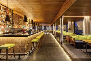 A bar area with stools and a counter, a seating area with couches and chairs, and a wooden ceiling. - Hotel Ambassador by ACE Hotels, Kathmandu. (Kathmandu)