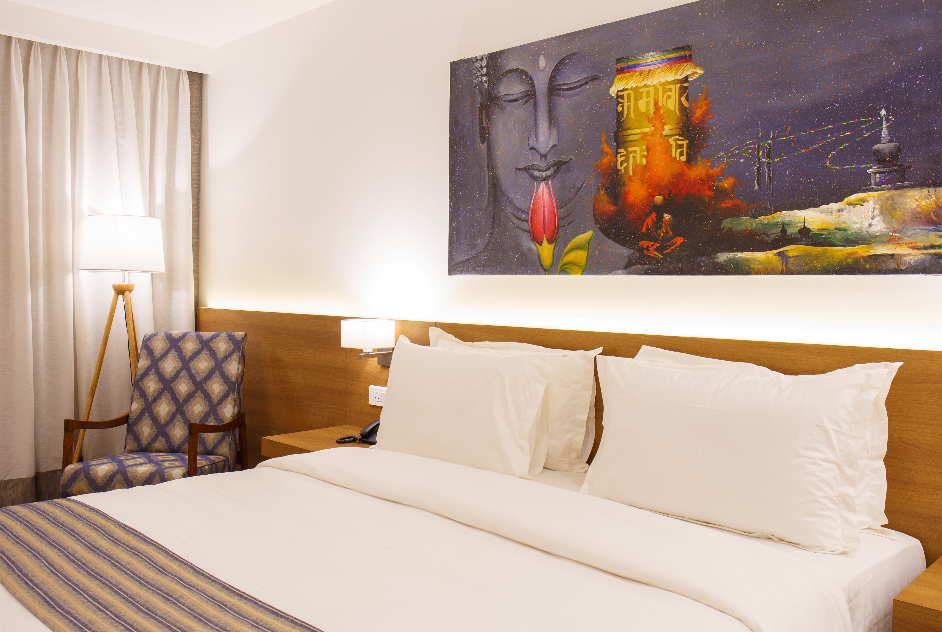 A hotel room with a large bed, a chair, a lamp, and a painting on the wall.
