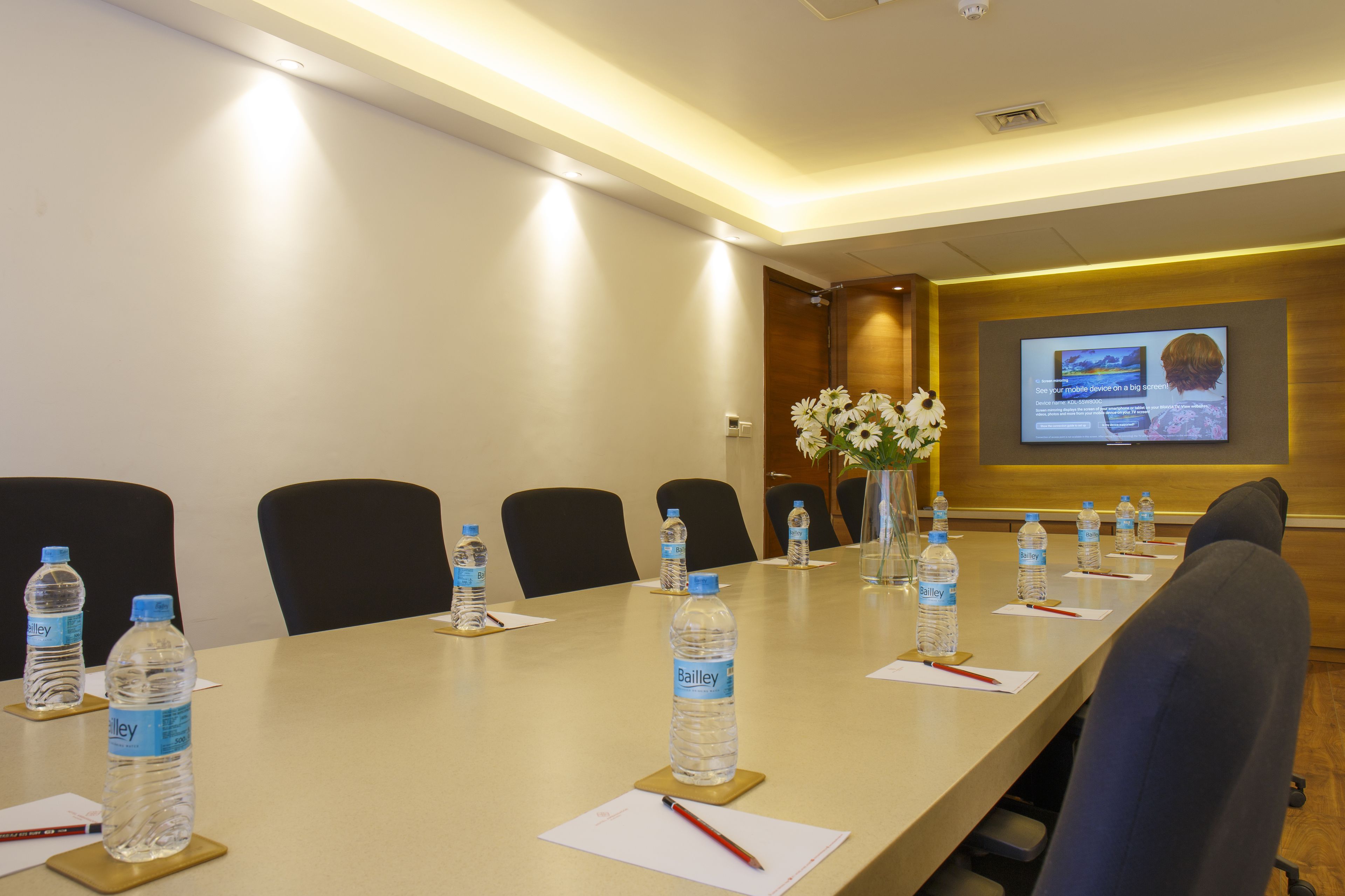 A conference room with a long table, water bottles, and a projector screen displaying a presentation.