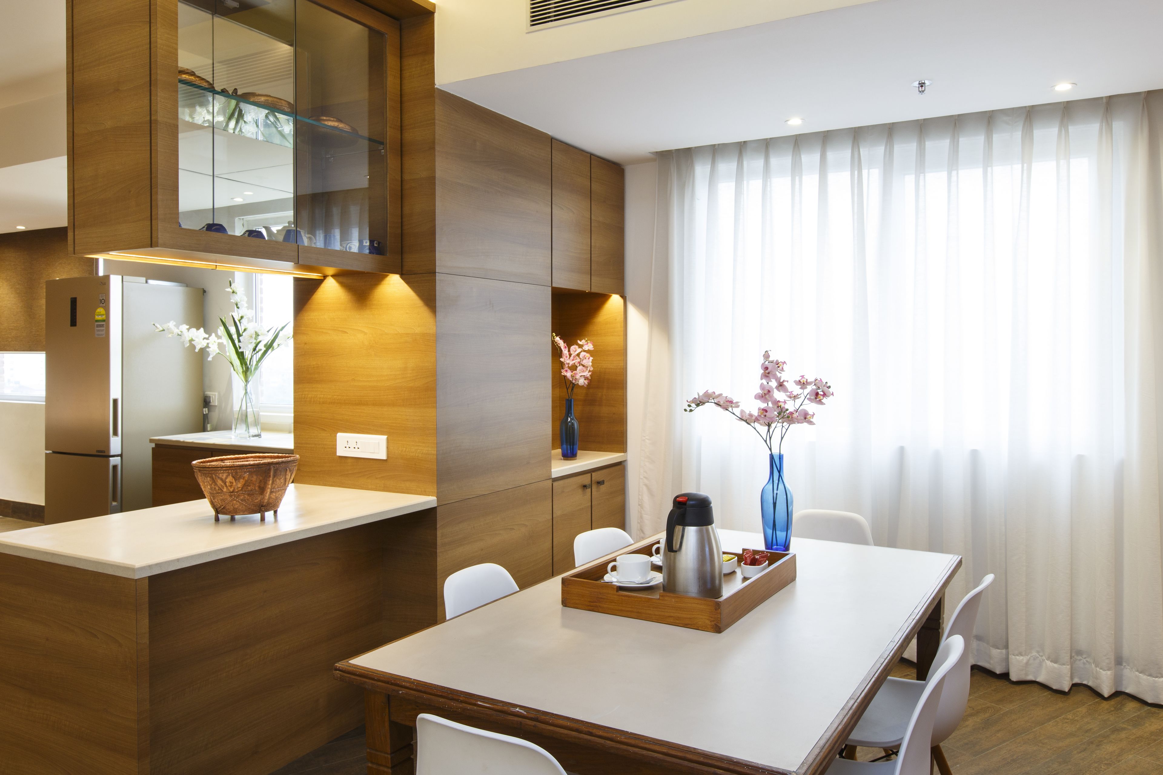 Una cocina moderna con armarios de madera, encimera blanca y un comedor con mesa y sillas blancas.