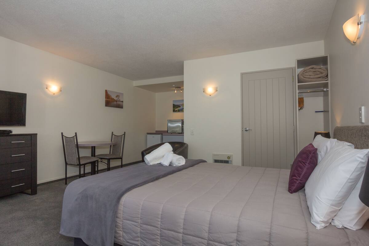 A bedroom with a bed, a desk, a chair, a television, and a closet.