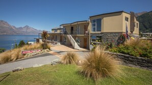Ein modernes, zweistöckiges Haus mit Natursteinfassade, einem Balkon und Blick auf einen See und Berge.