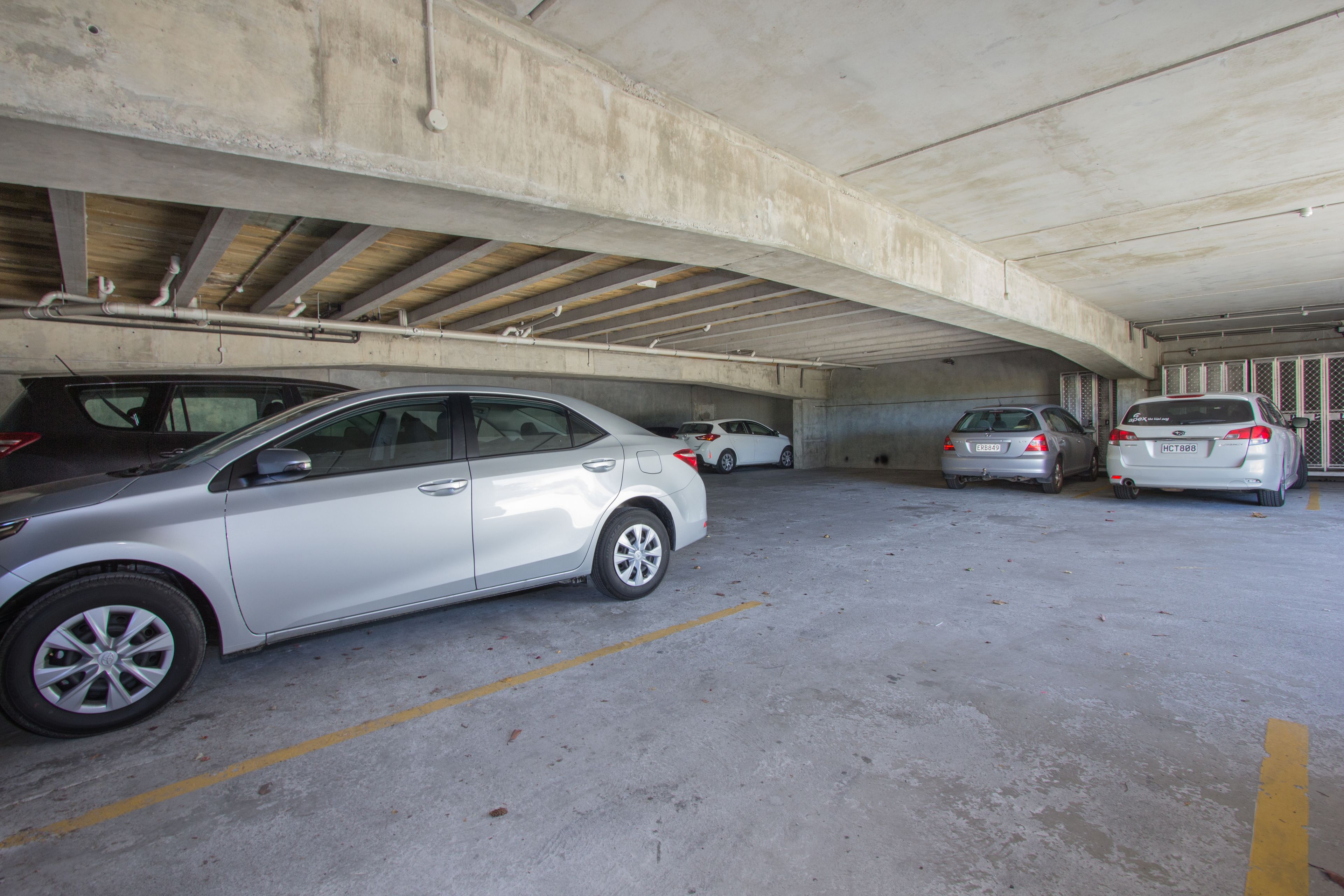 Een parkeergarage met betonnen plafonds en muren, meerdere geparkeerde auto's en zichtbare dragers.
