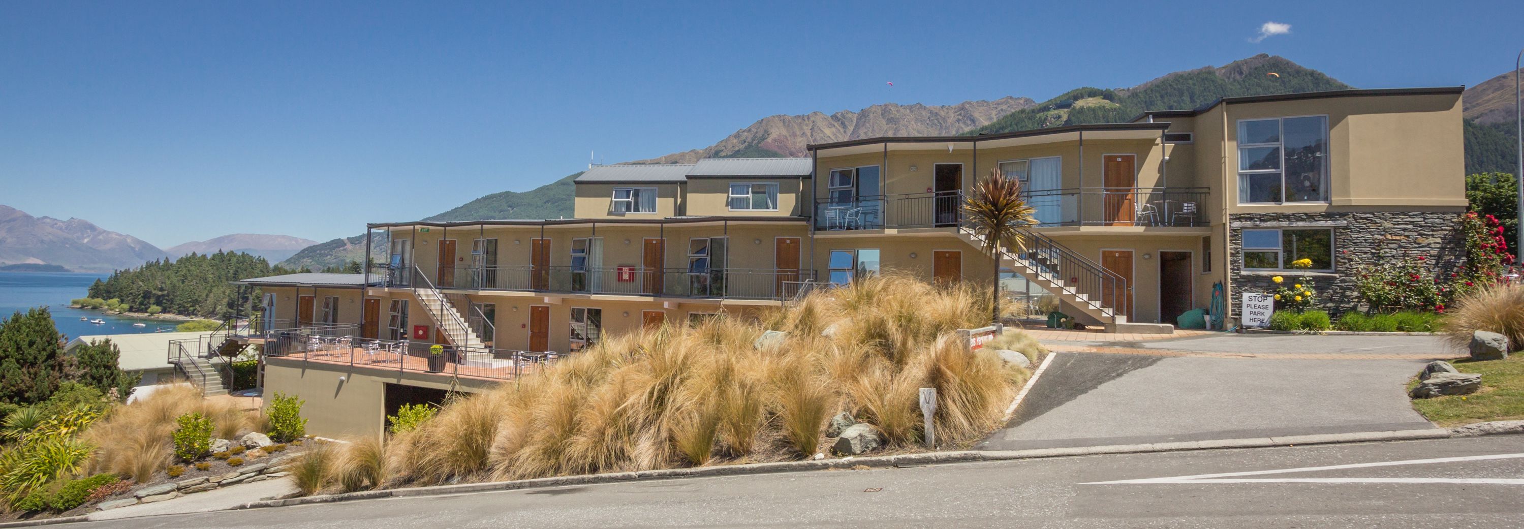 Un hotel de varios pisos con piscina, situado cerca de un lago con montañas al fondo.
