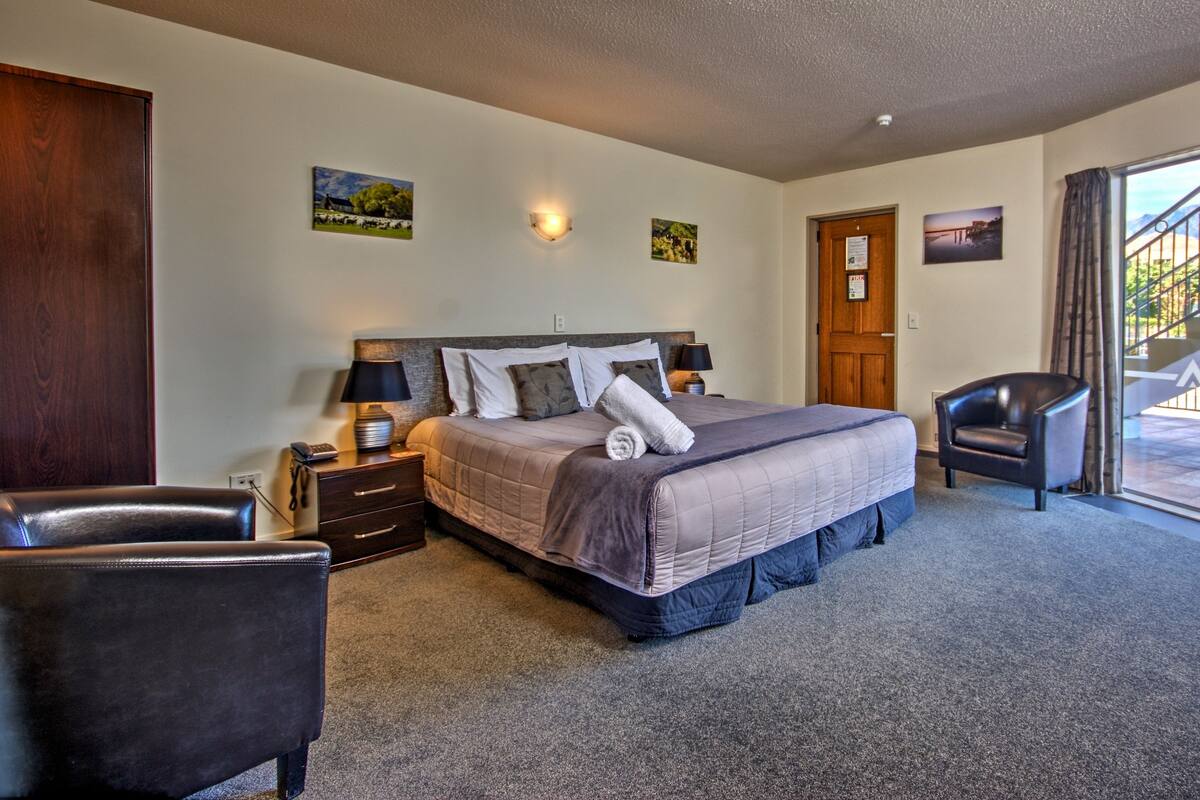 A bedroom with a large bed, a chair, a nightstand, and a door leading to a balcony.