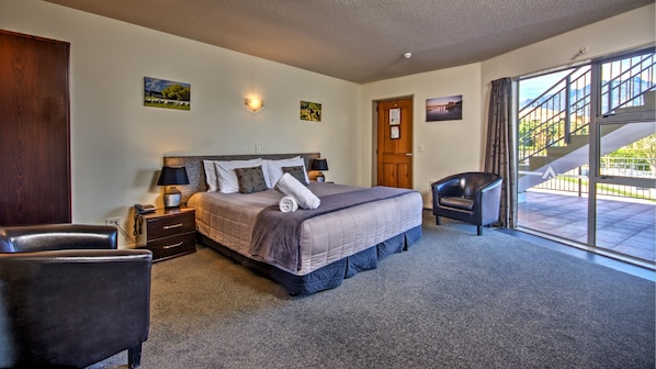 A bedroom with a large bed, a chair, a nightstand, and a door leading to a balcony. - Alexis Motels & Apartments (Queenstown)
