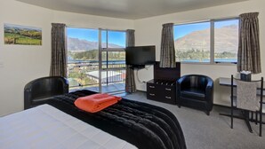 Ein Hotelzimmer mit einem Bett, einem Schreibtisch, zwei Stühlen, einem Fernseher und großen Fenstern mit Blick auf die Berge.