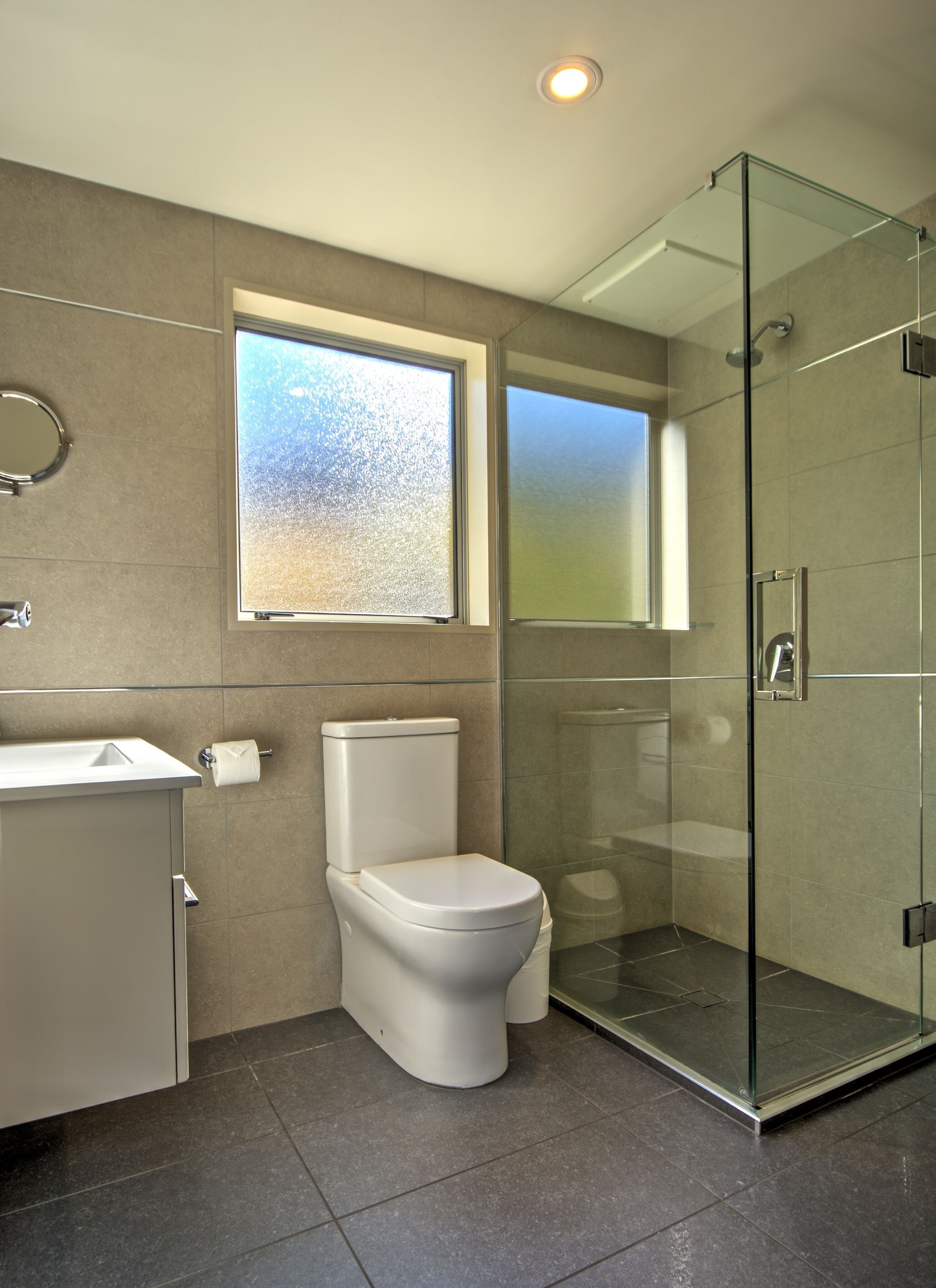 A modern bathroom with a toilet, a glass shower enclosure, and a window providing natural light.