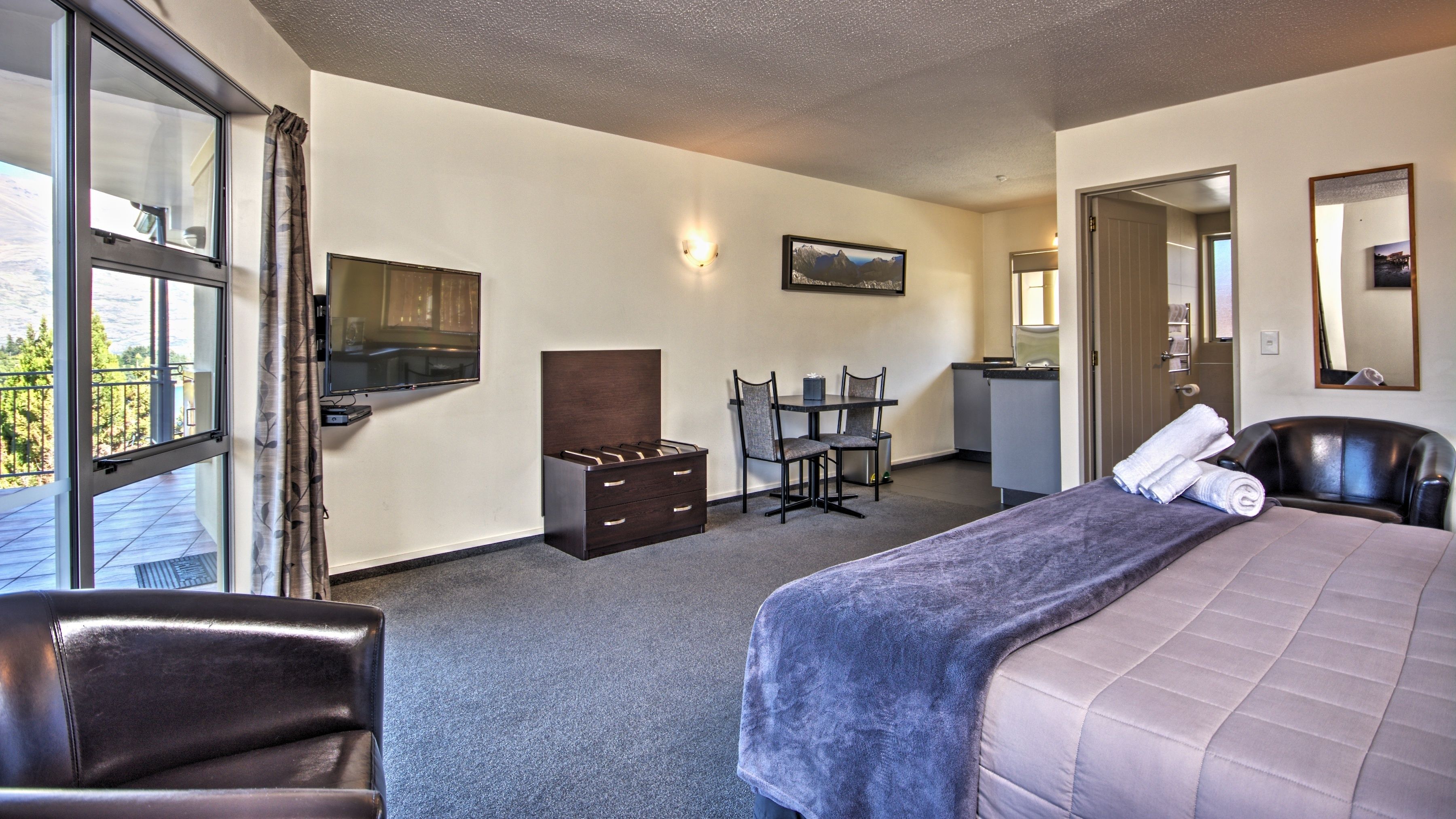 Ein Hotelzimmer mit Bett, Schreibtisch, Stuhl, Kommode und Fernseher.