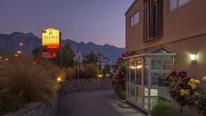 Ein Motel mit Eingangsbereich, Hinweisschild auf freie Zimmer, Bergelandschaft im Hintergrund und einem gut beleuchteten Empfangsbereich.