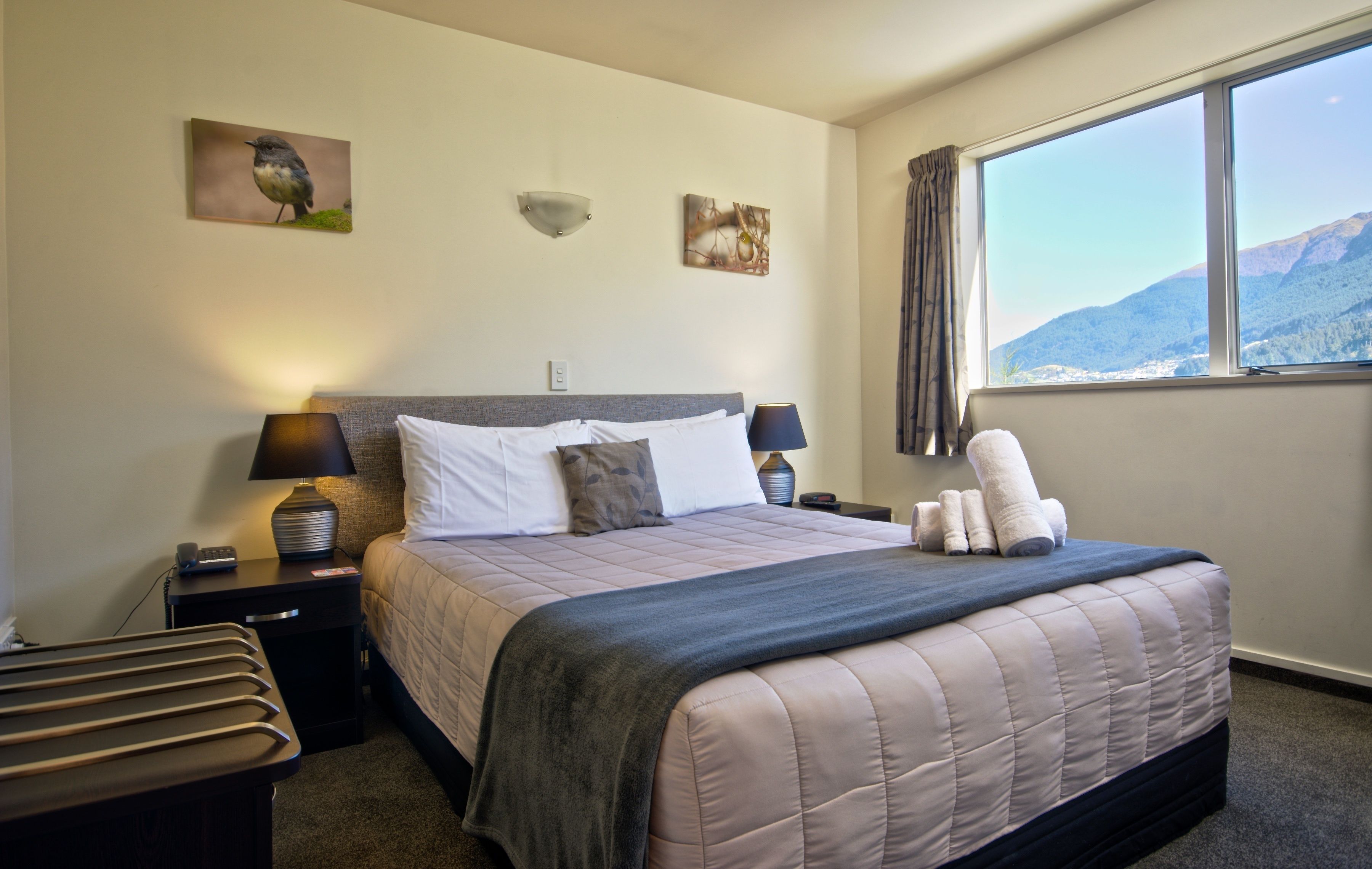 A neatly made bed with a quilt, two bedside lamps, a nightstand with a phone, and a window with a mountain view.