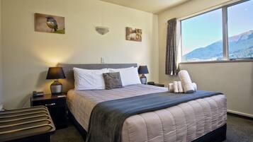 A neatly made bed with a quilt, two bedside lamps, a nightstand with a phone, and a window with a mountain view.