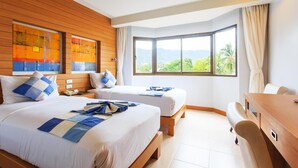 A hotel room with two beds, a desk, and a large window offering a view of greenery and mountains.