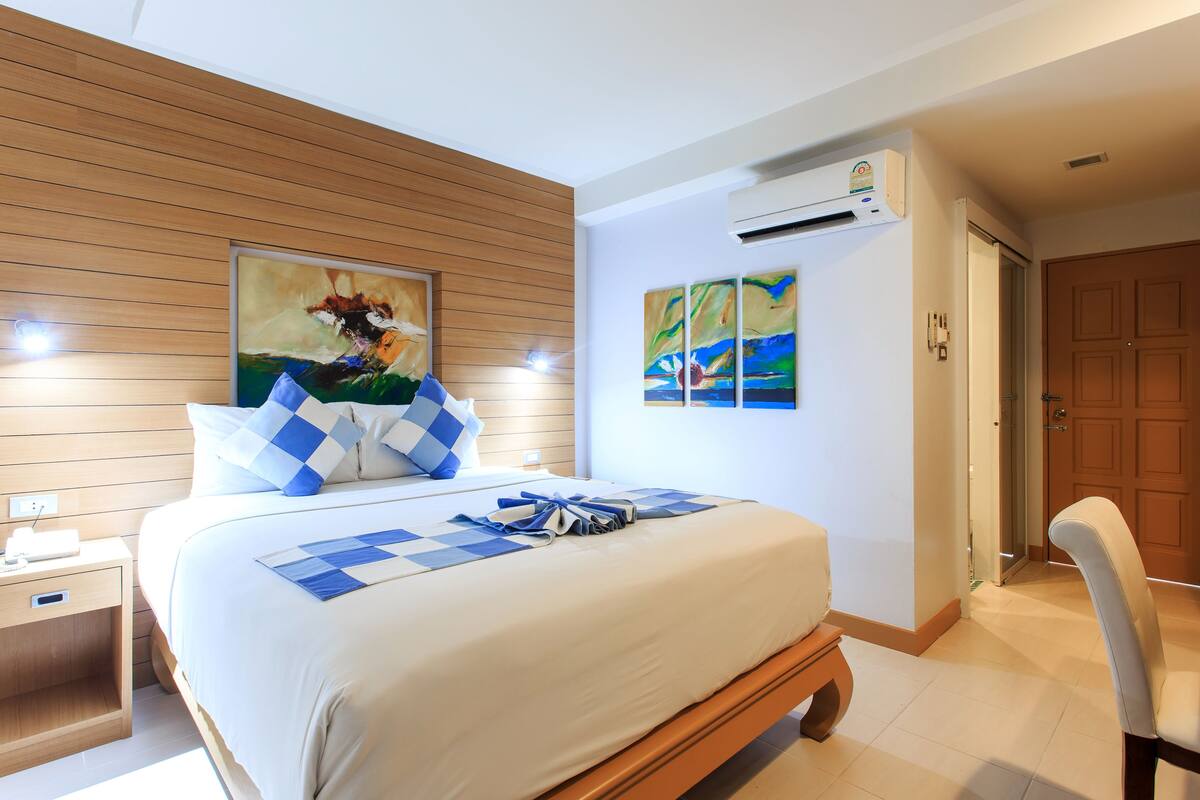 Ein Hotelzimmer mit Bett, Holz-Kopfteil, Bildern an den Wänden, einer Klimaanlage und einer Tür.