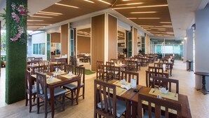 A spacious dining area with wooden tables and chairs, a green vertical garden, and a modern ceiling design.