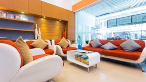 A modern lounge area with white and orange sofas, a coffee table with books, and a large window with a view of the city.