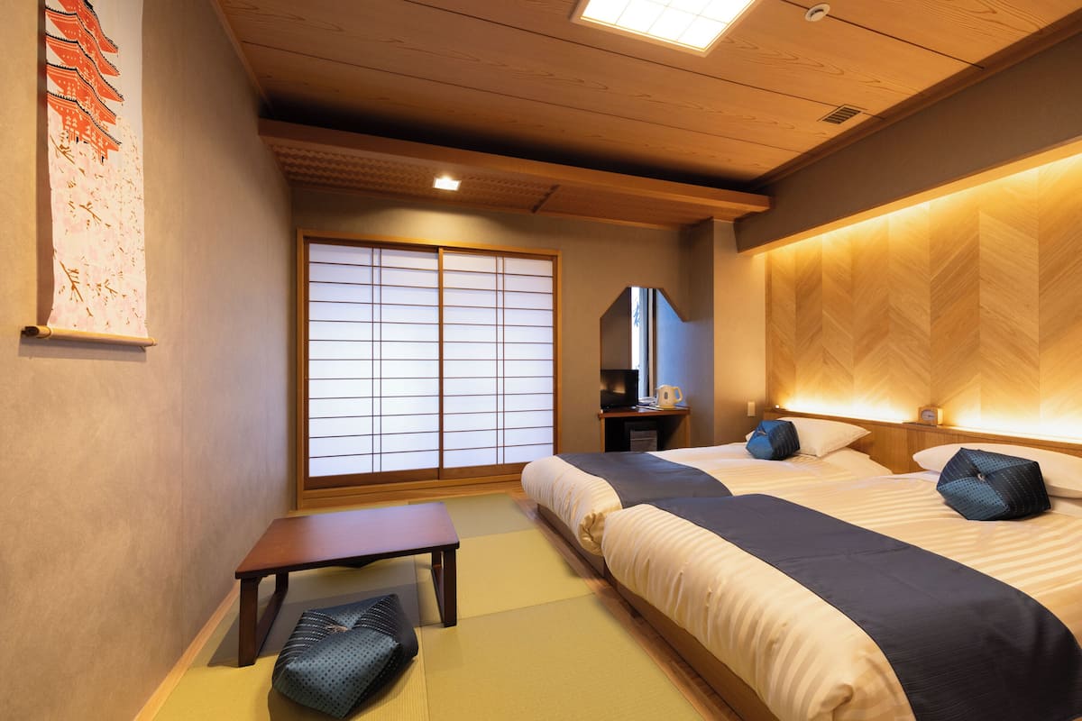 A traditional Japanese-style hotel room with tatami flooring, a shoji screen, and a bed with a wooden headboard.