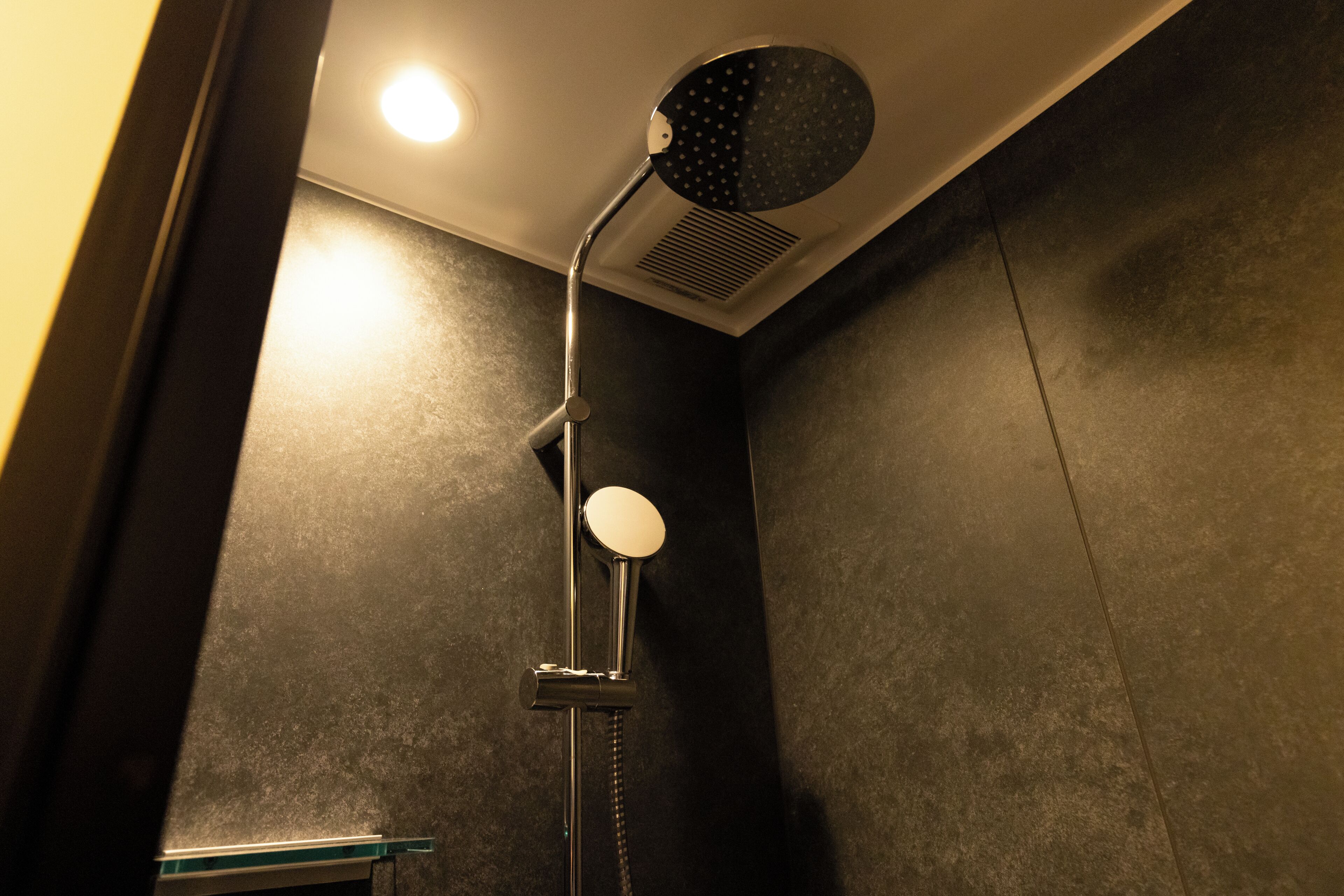 A shower with a round mirror, a handheld showerhead, and a wall-mounted control panel.
