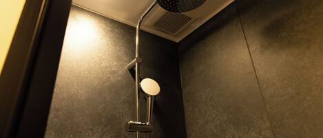A shower with a round mirror, a handheld showerhead, and a wall-mounted control panel.