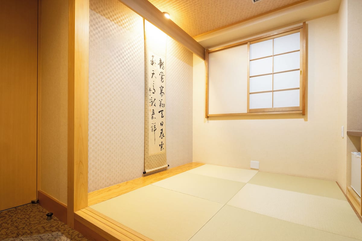 A traditional Japanese room with tatami flooring, a sliding door with calligraphy, and a window with wooden frames.