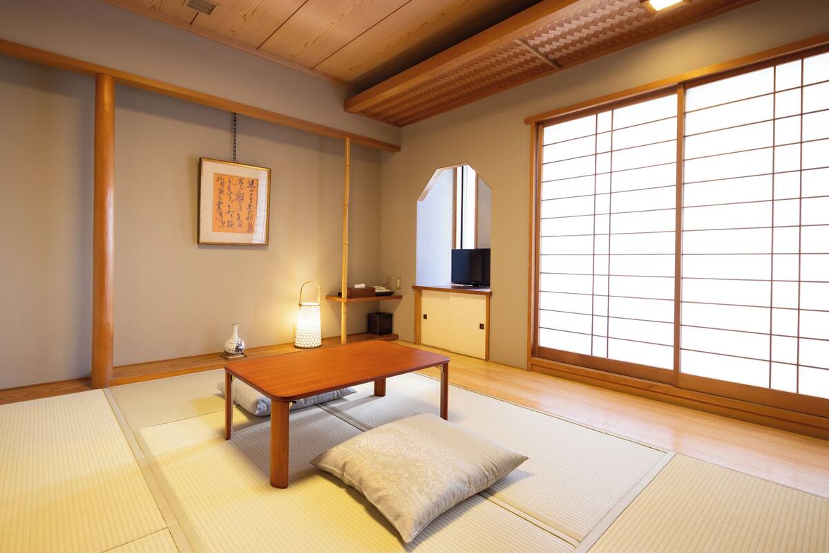 A traditional Japanese room with tatami flooring, a low wooden table, a cushion, a hanging picture, and sliding doors.