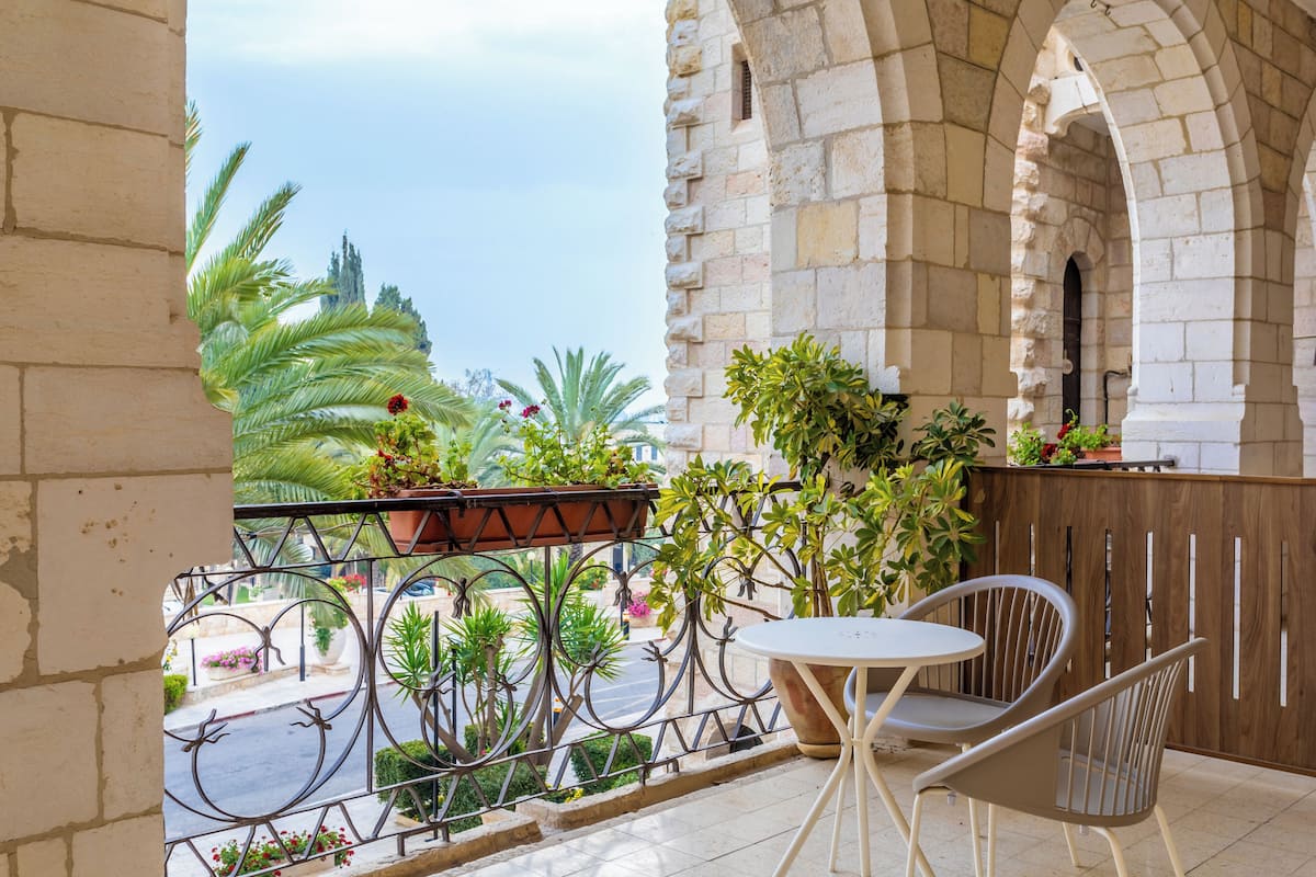A balcony with a table and chairs, surrounded by potted plants and a stone wall.