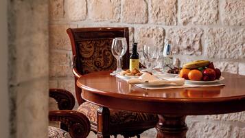 Una mesa redonda de madera con un plato de fruta y dos copas de vino, frente a una pared de piedra.