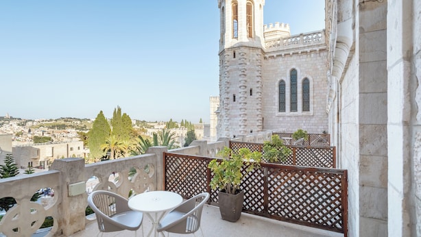 A balcony with a table and chairs, overlooking a historic building with a tower. - Notre Dame of Jerusalem Center (Jerusalem)