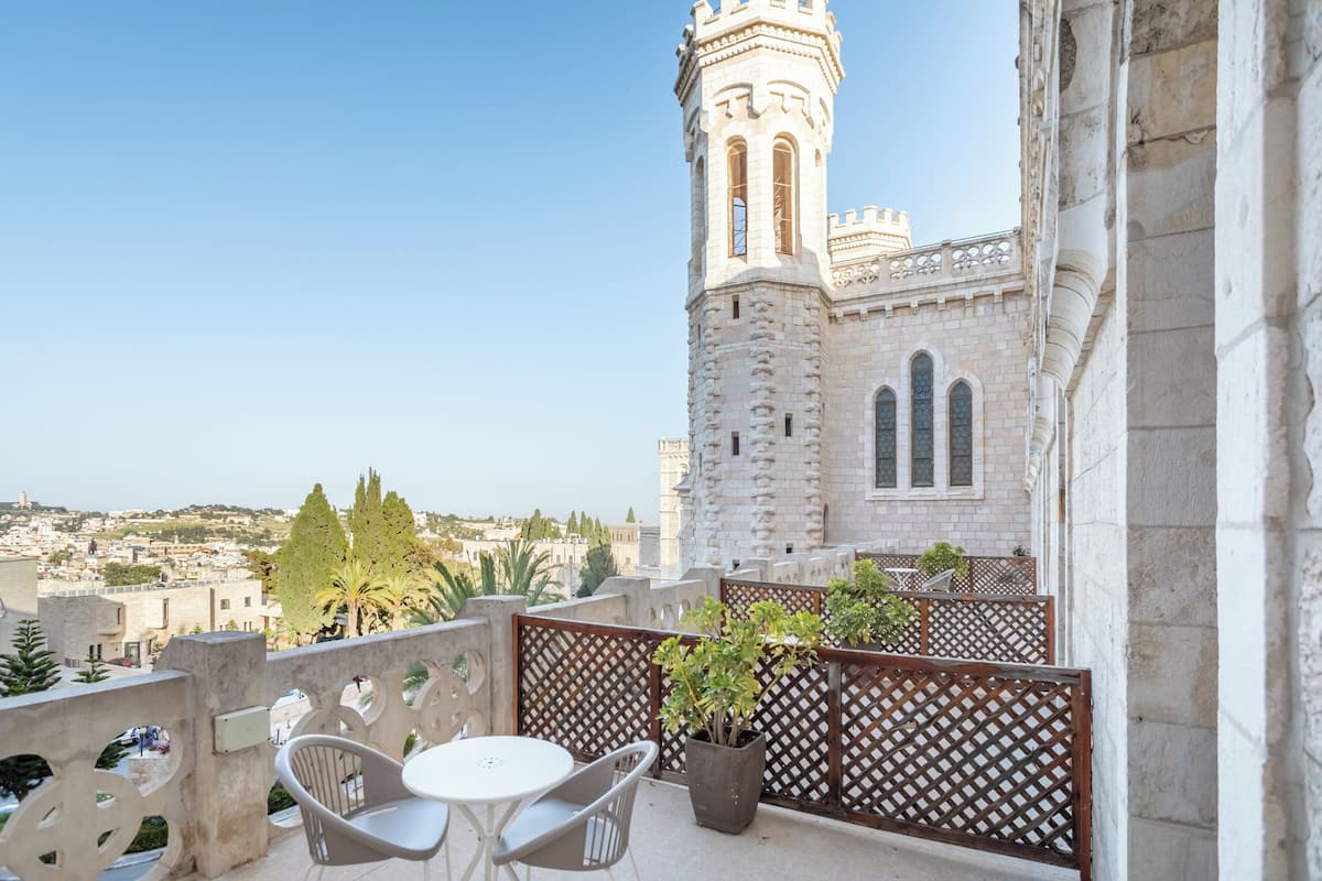 A balcony with a table and chairs, overlooking a historic building with a tower.