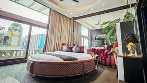 A spacious bedroom with a large bed, a ceiling fan, and a city view through large windows.