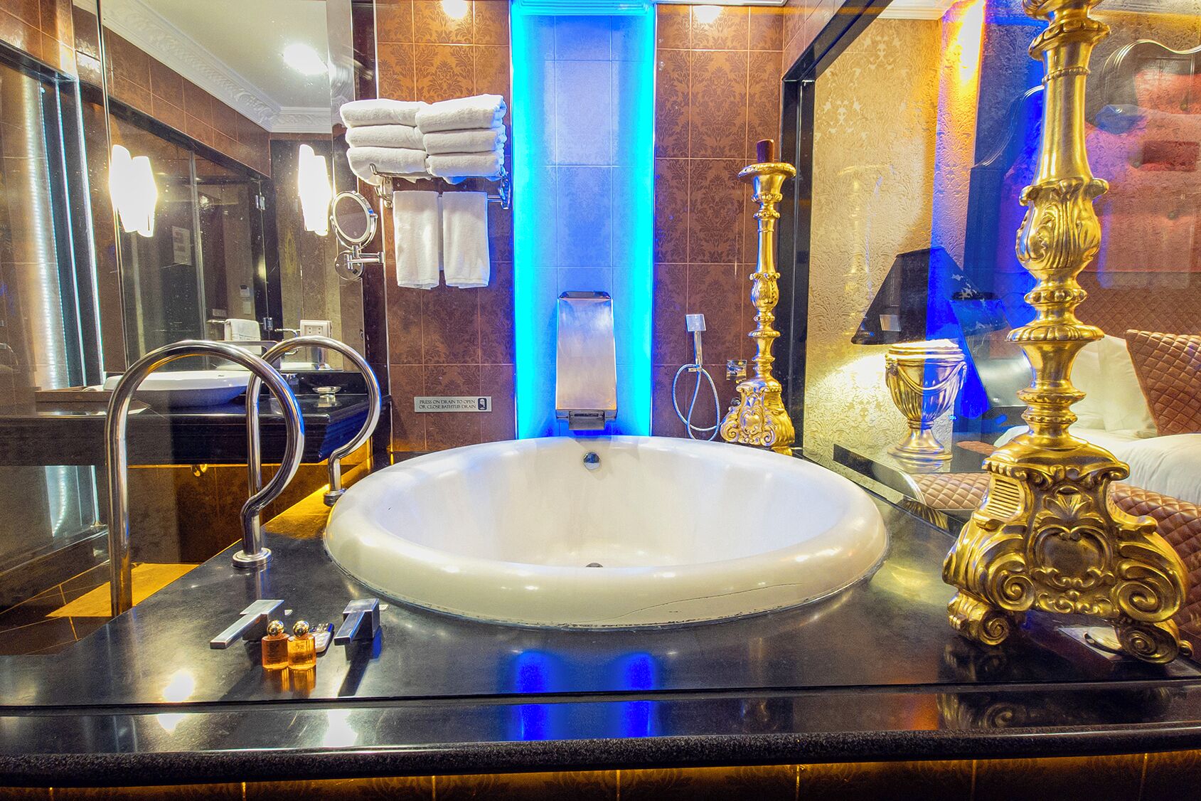 A luxurious bathroom with a large white sink, gold fixtures, and a mirror reflecting the room.