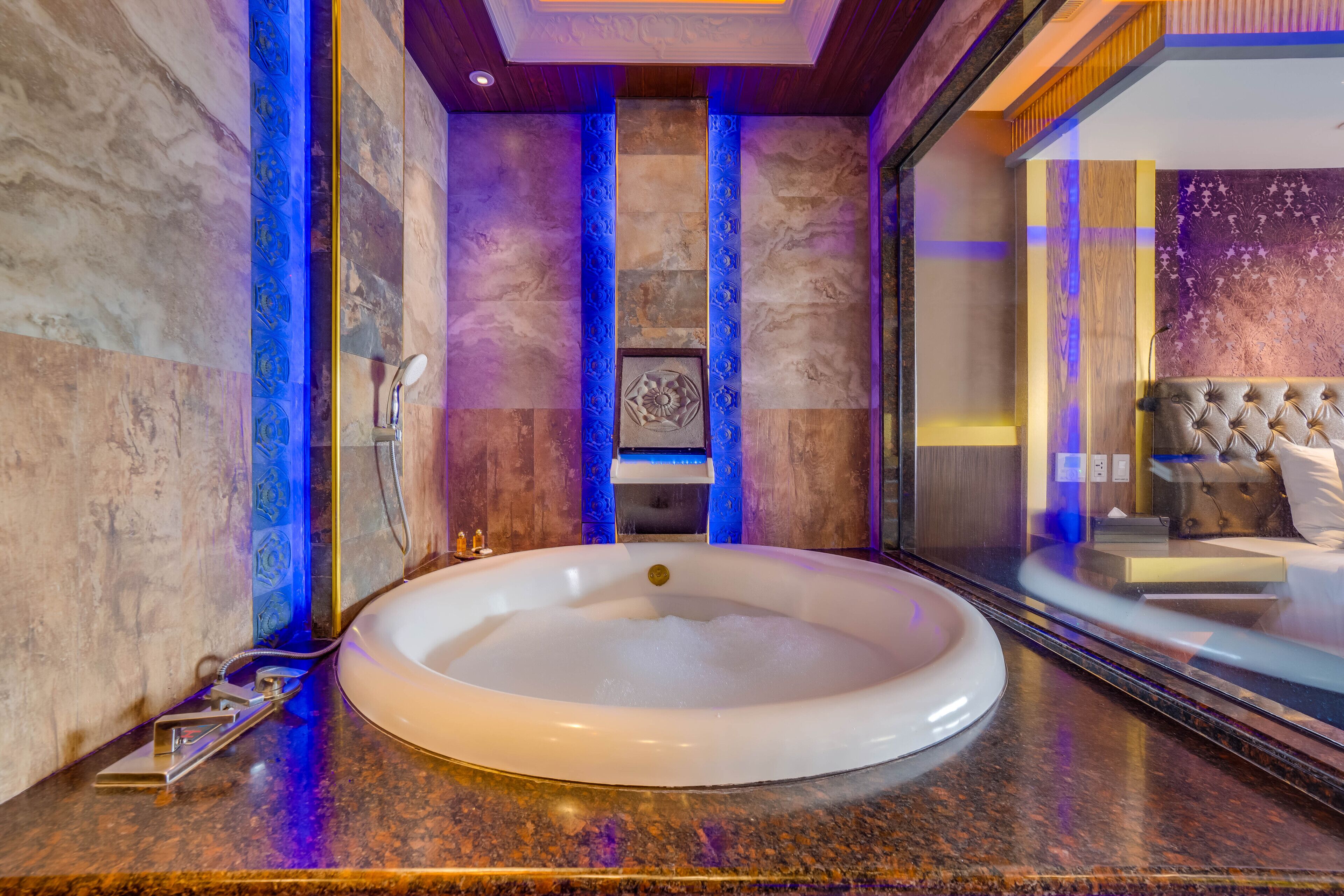 Une salle de bain luxueuse avec une baignoire sur pieds, des murs en marbre et une vue sur une chambre à coucher dotée d’une tête de lit capitonnée.