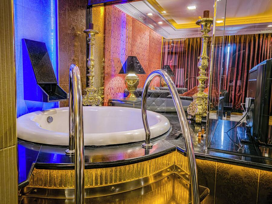 Un baño lujoso con una bañera grande, ornamentales accesorios dorados y un espejo que refleja la decoración de la habitación.