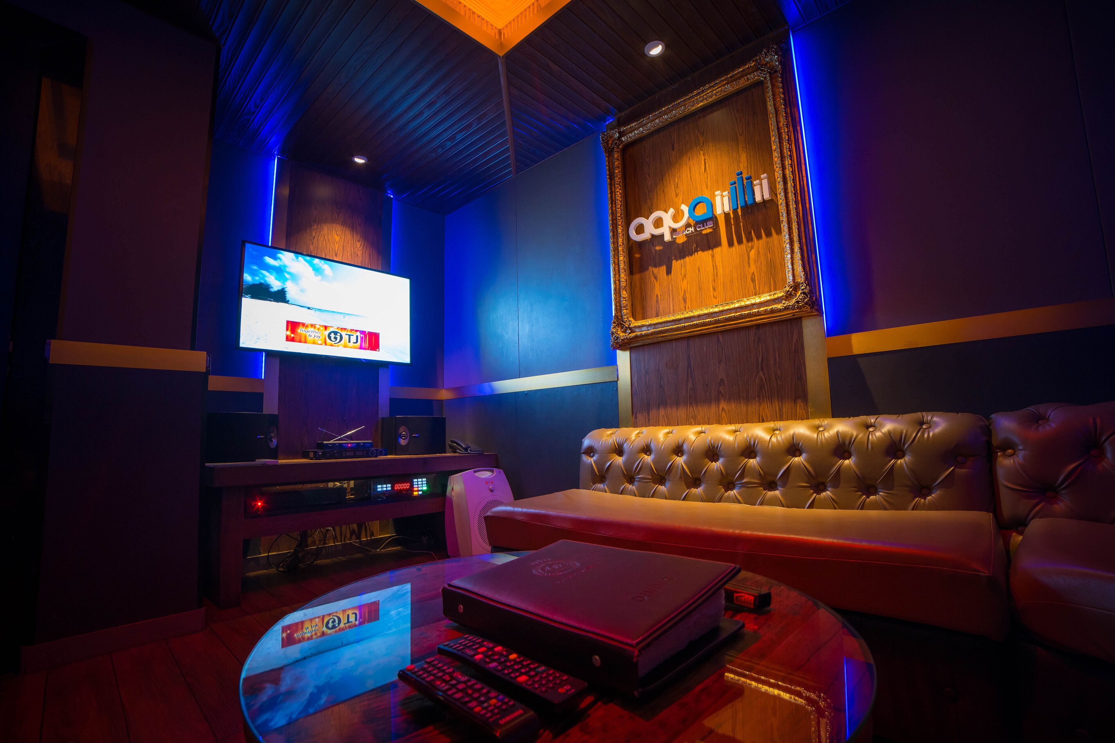 A room with a large screen, a sofa, a gaming console, and a wooden wall with a sign.