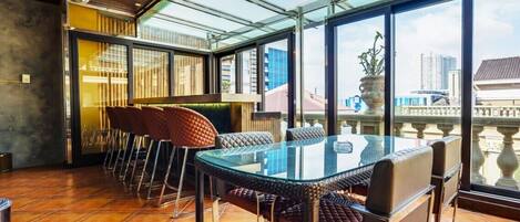 A modern dining area with a glass table and chairs, a view of the city through large windows, and a balcony with a railing.