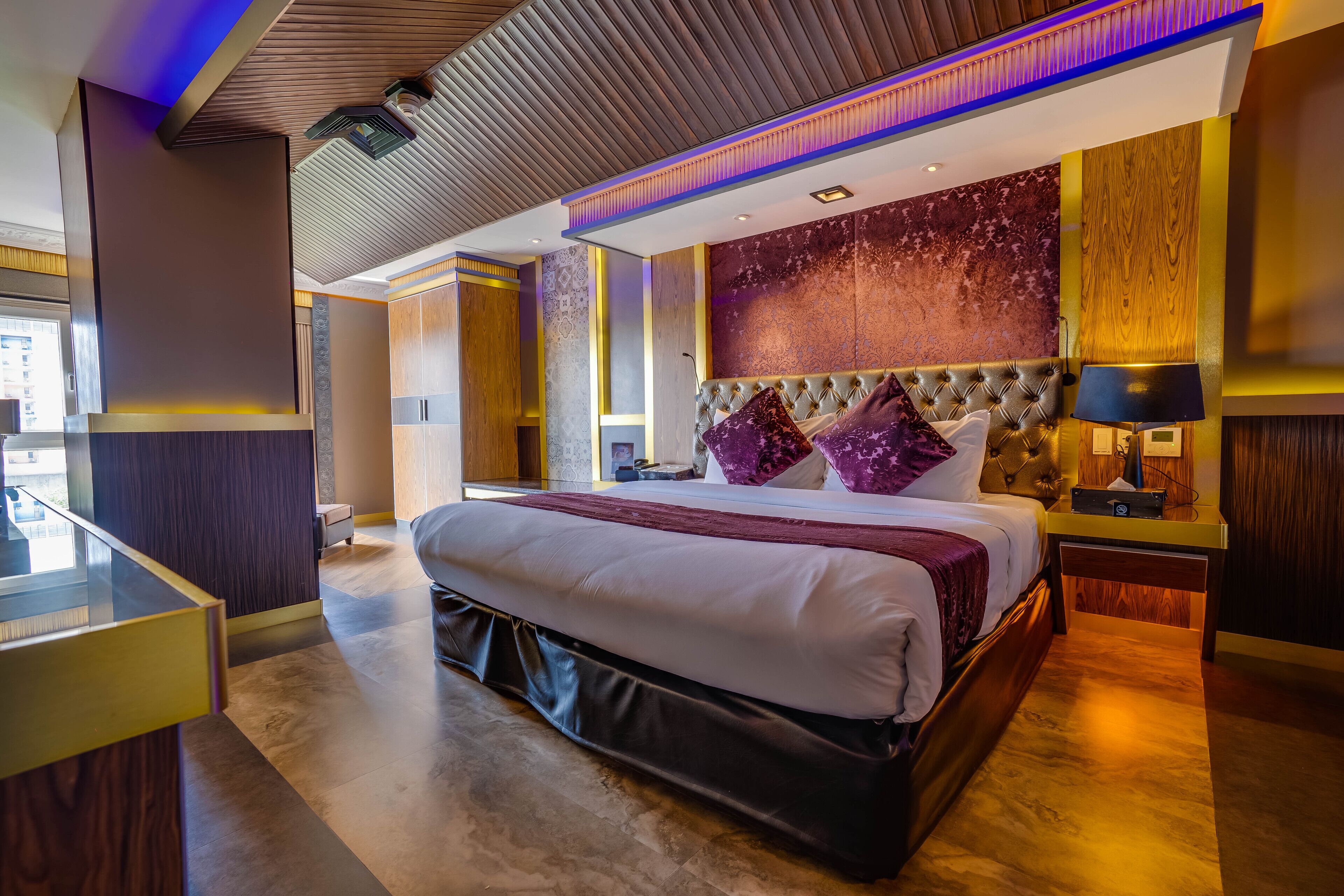 A modern hotel room with a large bed, a wooden headboard, a marble-patterned wall, and a glass partition.